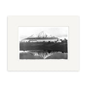 The Mt Taranaki 1900 - HI144 is a black and white illustration of New Zealand’s snow-capped Mt Taranaki with buildings at its base, reflected in still water. This historical photographic print comes centered on an archival quality white mat.