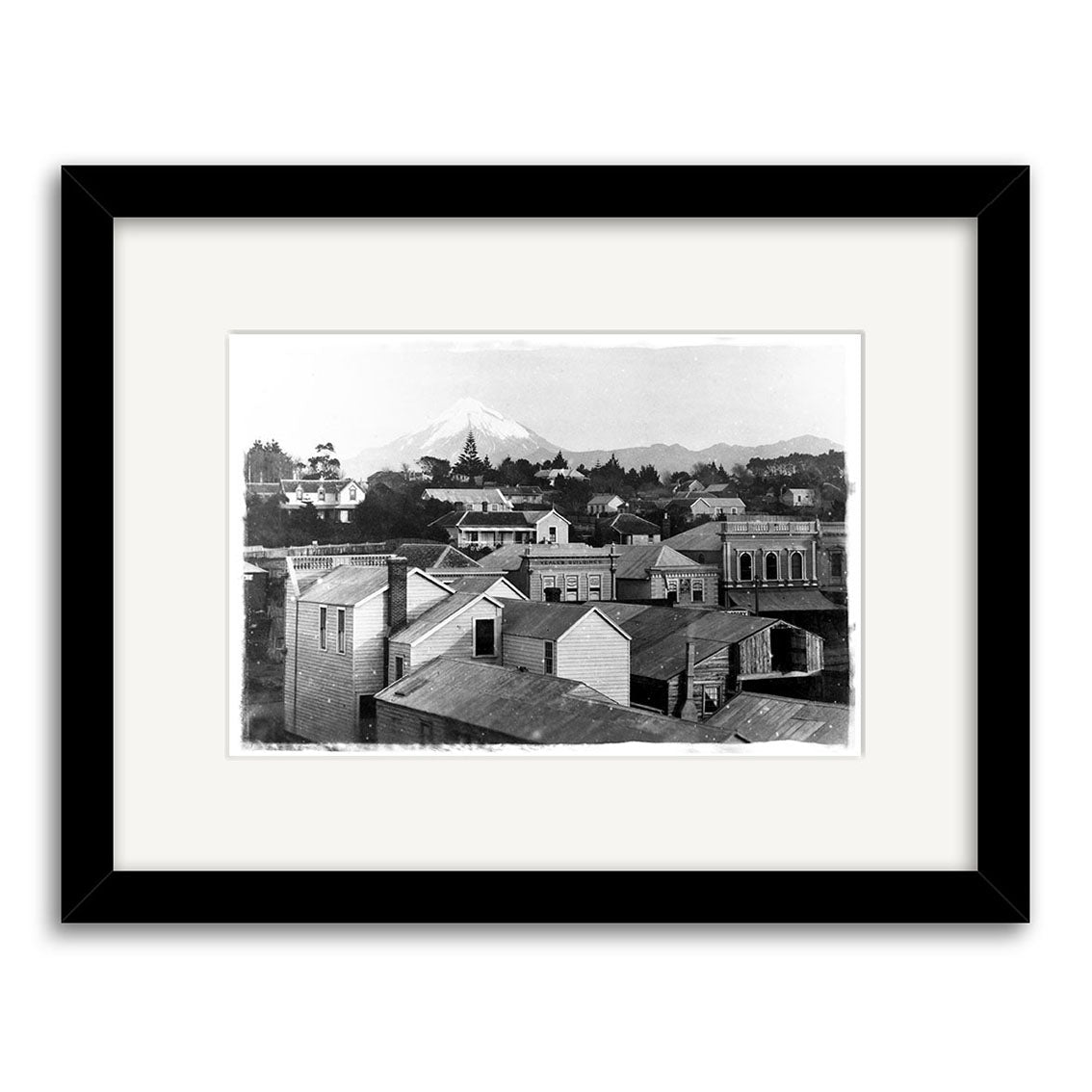 Mt Taranaki 1881 - HI145: Black and white historical photo print of a small town with wooden buildings and a snowy mountain, framed in black with white mat, printed on archival quality matte paper.