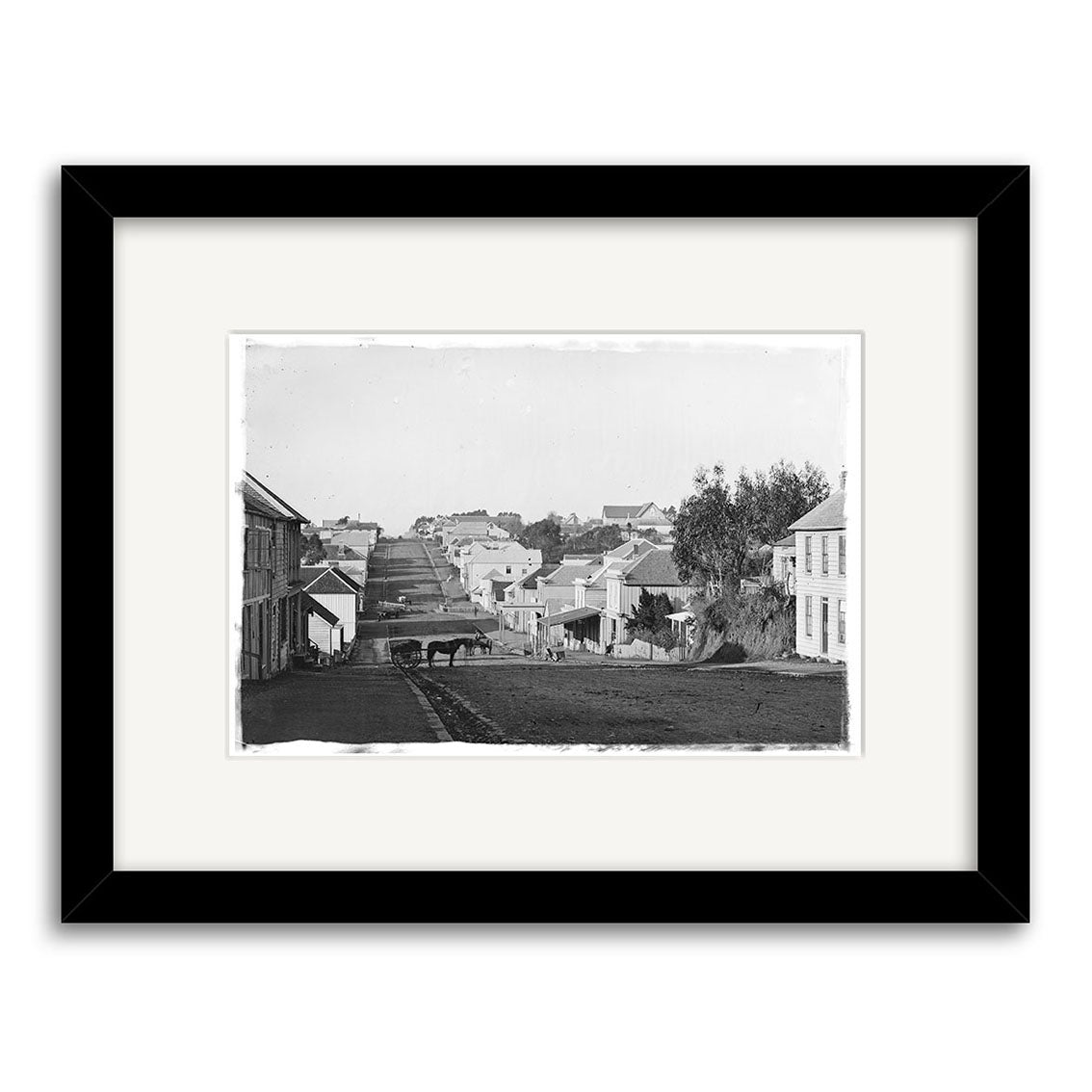 Devon St 1860 - HI146 is a black-and-white photo in a black frame, depicting a quiet street with houses and a horse-drawn cart. This historical print is made in New Zealand on archival quality matte paper.