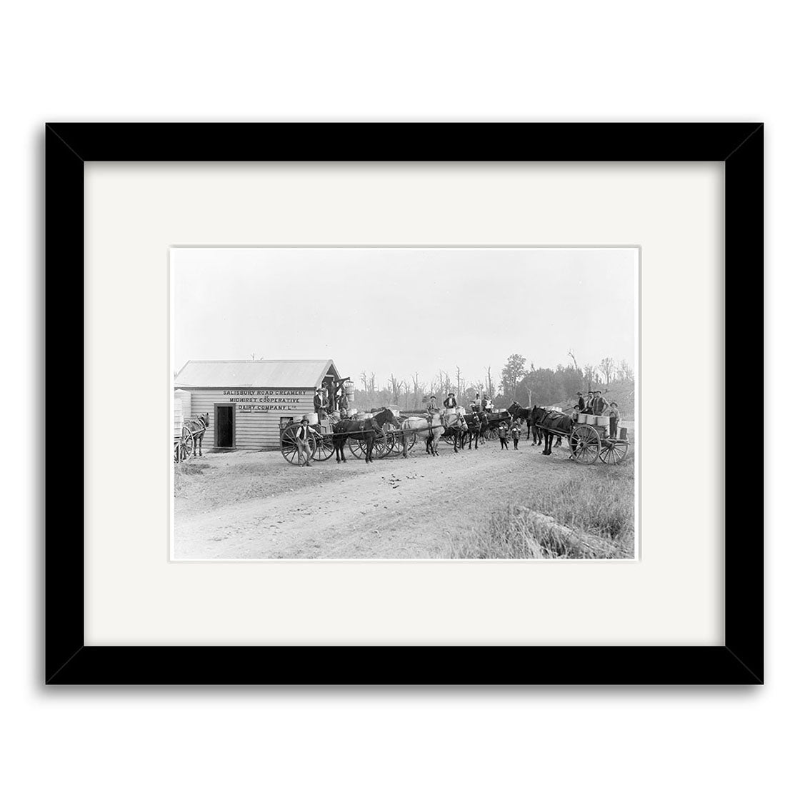 Archival-quality black-and-white photographic print titled Salisbury Rd 1900 - HI148 shows horse-drawn carriages and people by a wooden building on a dirt road in New Zealand, with trees in the background.