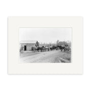 Archival black-and-white photographic print, Salisbury Rd 1900 - HI148, shows horse-drawn carriages stopped by a small wooden building, with people gathered on a dirt road and trees framing the scene in New Zealand.