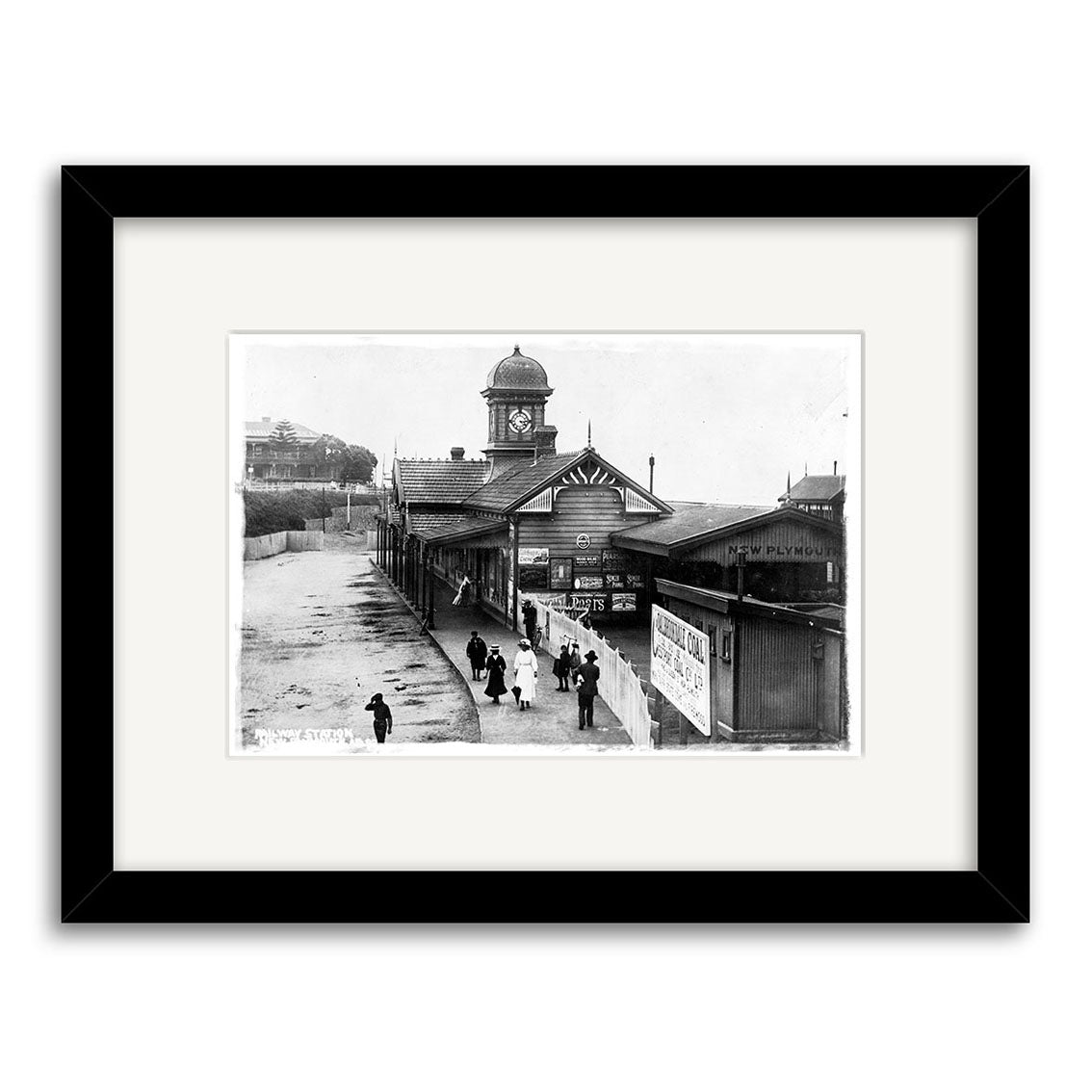 Black and white historical photographic print of New Plymouth Railway Station 1900 (HI151), featuring a clock tower, covered platforms, and people. Framed with a white mat and black frame on archival matte paper. Made in New Zealand.