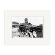 The New Plymouth Railway Station 1900 - HI151 is a black and white historical print showing a platform with people, a station building with clock tower and wall ads. Printed on archival matte paper, made in New Zealand.