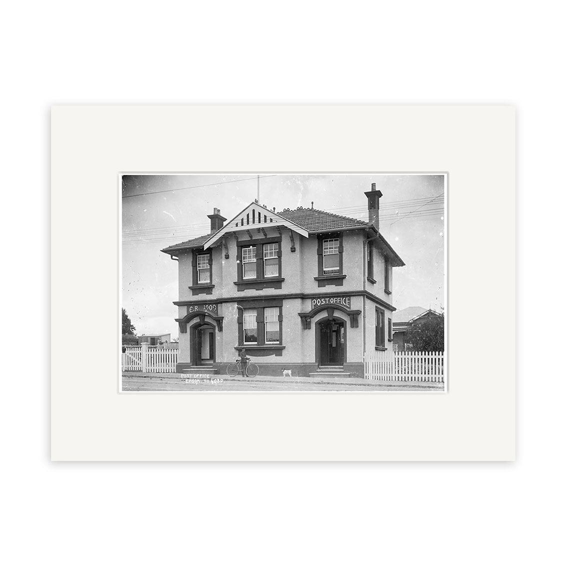 A historical 1910 print of Epsom Post Office (HI154), showing a two-story building, bicycle in front, picket fences, and houses behind. Printed on archival matte paper. A beautiful piece of New Zealand heritage.
