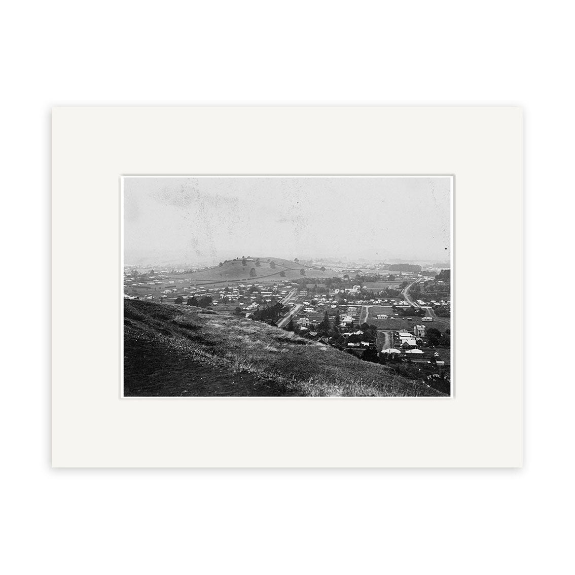 Archival quality black and white photo Epsom 1907 No.2 - HI159 shows a New Zealand town with houses and streets viewed from a hillside, larger hill and open land in the background, matted with a white border.