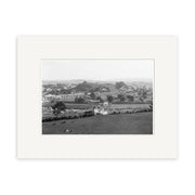 The Epsom 1909 - HI160 is a black and white archival matte print showing a rural landscape with scattered houses, open fields, roads, grazing animals in front, and distant hills and buildings.