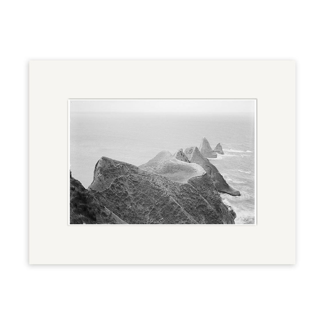 Cape Kidnappers 1880 - HI161: Historical black and white photo of dramatic triangular rock formations in the ocean, seen from above. Printed on archival matte paper, it captures the misty sea and rugged coastline.
