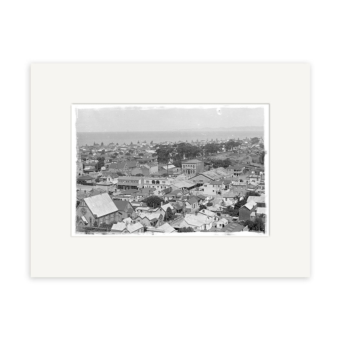 Black-and-white photograph titled Napier 1924 - HI163, showing densely built urban New Zealand with rooftops and low-rise buildings under a cloudy sky. This historical print comes matted in a white frame for archival preservation.