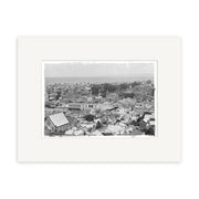 Black-and-white photograph titled Napier 1924 - HI163, showing densely built urban New Zealand with rooftops and low-rise buildings under a cloudy sky. This historical print comes matted in a white frame for archival preservation.