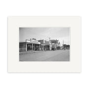 Black-and-white photo titled Havelock North 1925 - HI165 shows a small town street in New Zealand with storefronts, including a plumber’s shop, parked cars, bicycles, and people on the sidewalk; historical photographic print.