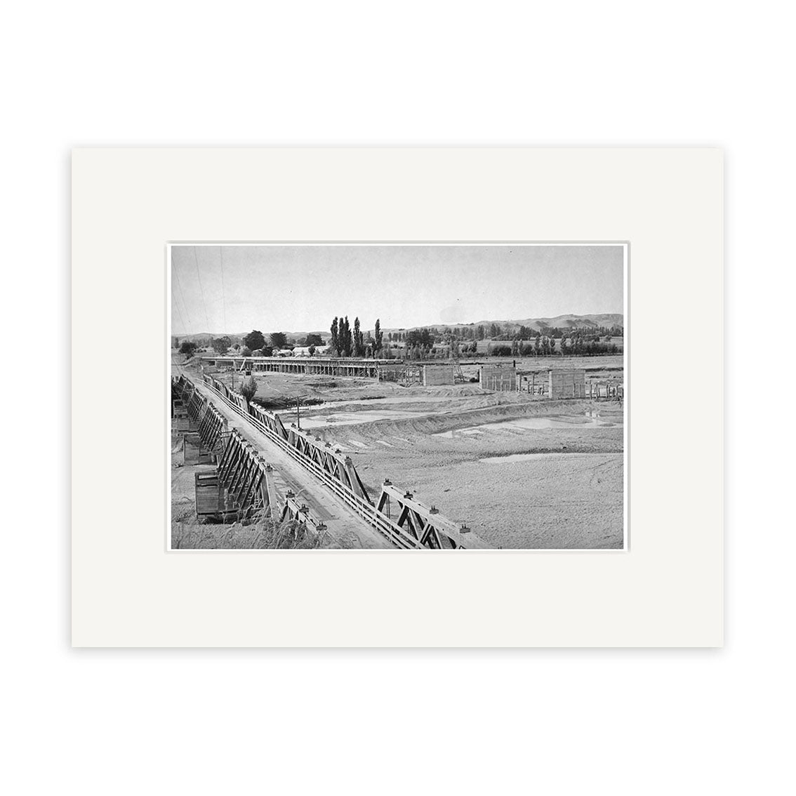 Black and white photo titled Hawkes Bay 1948 - HI166 shows a long wooden aqueduct crossing a barren landscape with distant trees, buildings, and faint mountains. Printed on matte paper for archival quality as a Historical Photographic Print.