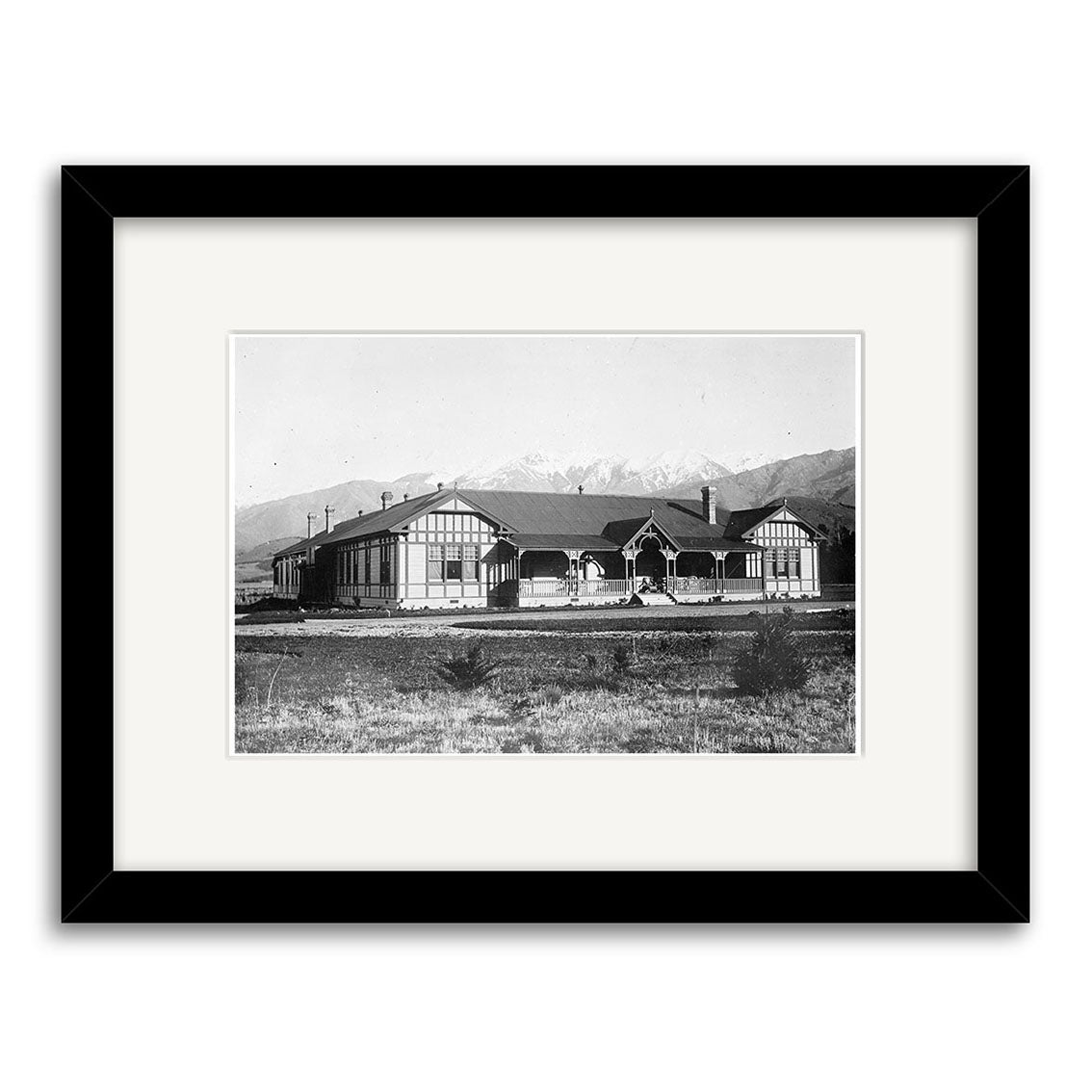 The Govt Sanatorium 1915 - HI171 is a black-and-white historical photographic print of a large, single-story building with gabled roof, set amid open land and mountains. Printed on archival matte paper and framed with white mat, black border.