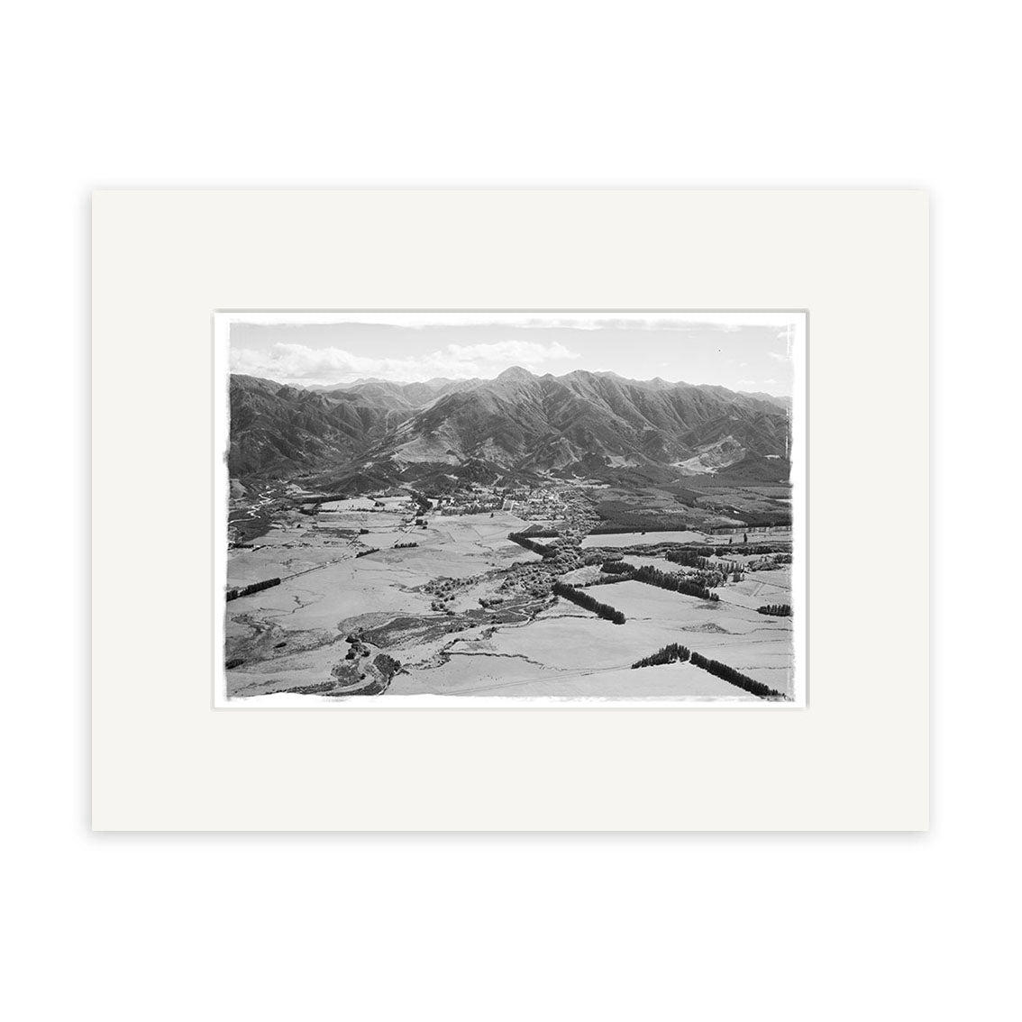 Black and white aerial photo titled Hanmer 1959 - HI172 shows fields, trees, a small town, and mountains. This historical print is framed with a white mat on archival-quality matte paper.