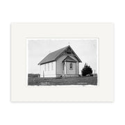 Archival-quality black and white photographic print of Catholic Church 1910 - HI175: a small wooden church with a steep metal roof, front porch, and crosses on top, standing on a grassy lot with a single tree. Made in New Zealand.