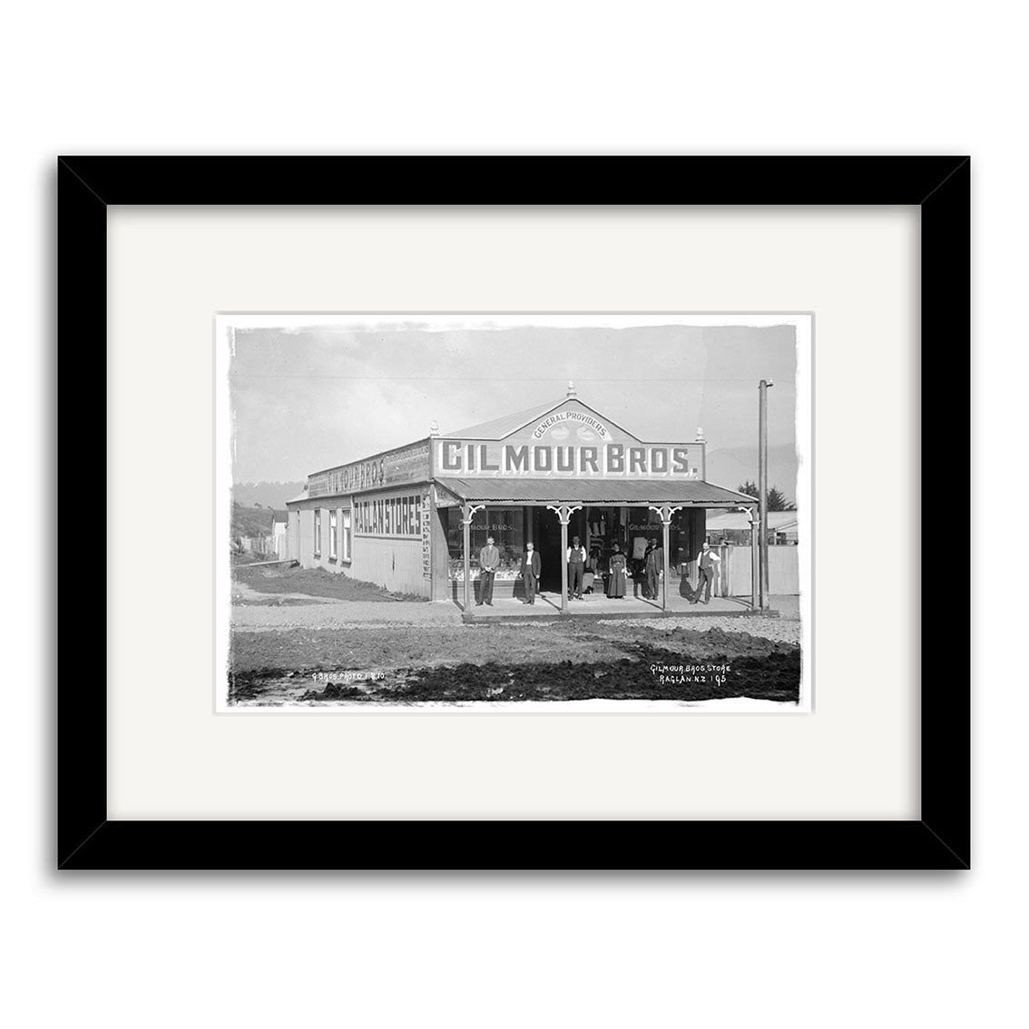 Gilmour Bros Store 1910 - HI177: Archival quality black and white photo of people outside the Gilmour Bros. building in New Zealand, advertising general merchants. Framed in black with a white mat.