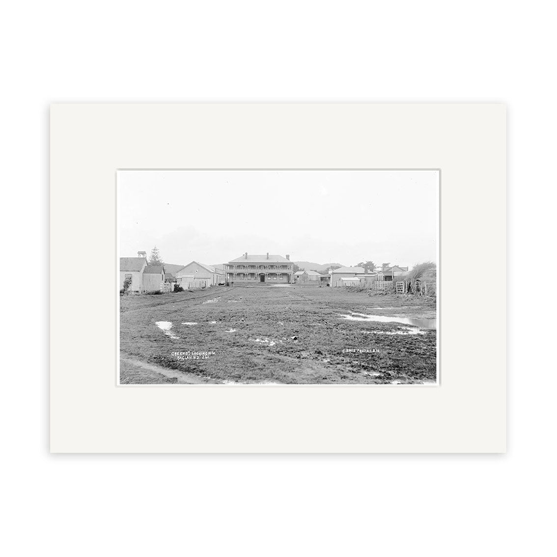 A black and white historical photographic print titled Green St Rangiora 1910 - HI178 on archival matte paper shows a muddy field, puddles, low buildings, fences, and a central structure in rural New Zealand.