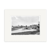 Main Street 1929 - HI180 is a black and white historical photographic print of a quiet, wide dirt street in a small New Zealand town with wooden buildings and trees. This archival-quality image features a white border on a white background.