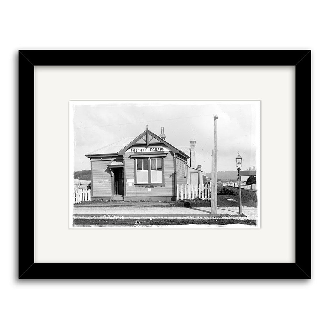 Black and white Historical Photographic Print titled Post Office 1910 - HI182 shows a small wooden building marked POST & TELEGRAPH, with picket fence and streetlamp, beautifully presented on archival quality matte paper.