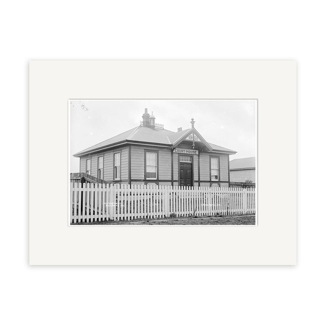 Raglan Court House 1910 - HI188: Black and white historical print of a small, gabled courthouse with picket fence and “Court House” sign, matted with a white border on archival quality matte paper.