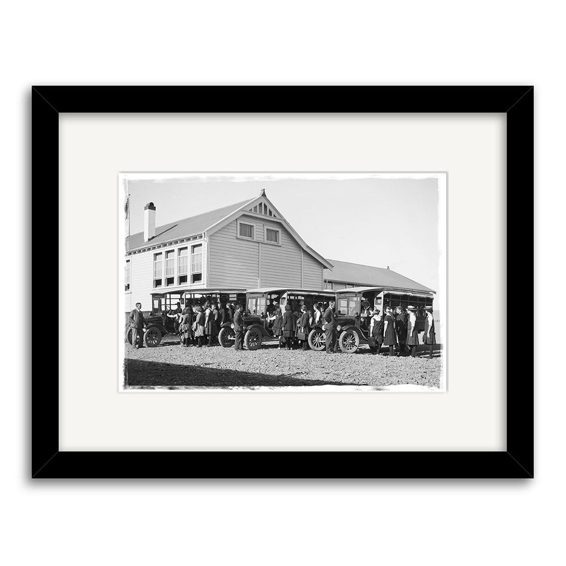 Archival-quality black-and-white print: Piopio School Waitomo 1924 No.1 - HI191 shows a group by early cars in front of a large wooden building in New Zealand, presented with archival matting and a classic black frame.