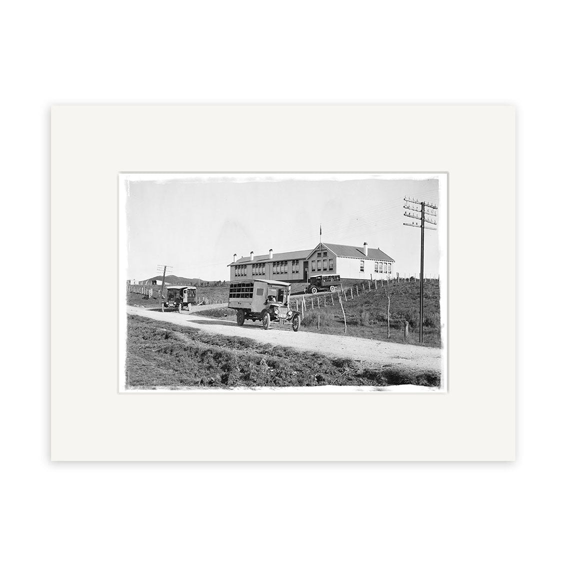 Archival quality black-and-white photo titled Piopio School Waitomo 1924 No.2 - HI192, showing early 20th-century automobiles on a dirt road by a two-story building with arched windows in rural New Zealand. Historical Photographic Print.