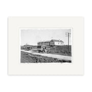 Archival quality black-and-white photo titled Piopio School Waitomo 1924 No.2 - HI192, showing early 20th-century automobiles on a dirt road by a two-story building with arched windows in rural New Zealand. Historical Photographic Print.