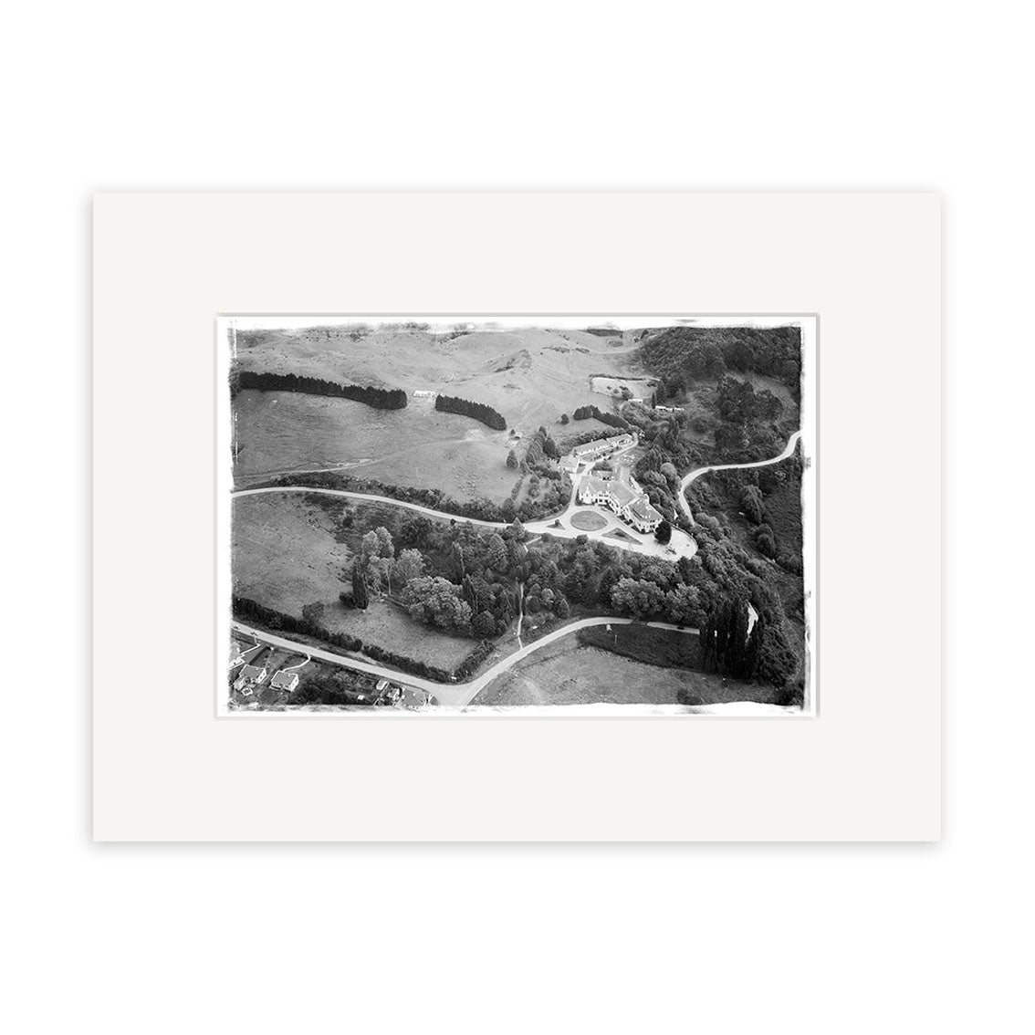 The Waitomo Caves 1955 - HI193 Historical Photographic Print features a black and white aerial view of rural New Zealand with winding roads, fields, and a central circular area. It is matted in white to enhance archival quality.
