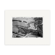 The Waitomo Caves 1955 - HI193 Historical Photographic Print features a black and white aerial view of rural New Zealand with winding roads, fields, and a central circular area. It is matted in white to enhance archival quality.