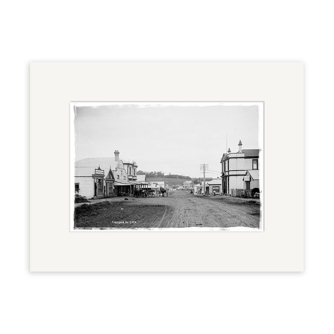 King Street 1909 - HI194: Black and white historical photographic print on matte archival paper shows a dirt road with wooden buildings and utility poles, capturing the spirit of a small town in the early 20th century.