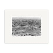 The Pukekohe 1963 - HI197 is a black and white aerial photo print of a racetrack amid fields and farmland, with scattered buildings and roads. The historical image comes matted with a plain white border.