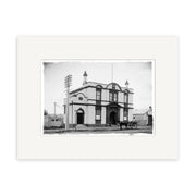 Black-and-white archival print: Pukekohe Post Office 1909 (HI198). Features a two-story building with arched windows, horse-drawn carriage, and telephone poles. Ideal for collectors of New Zealand history.
