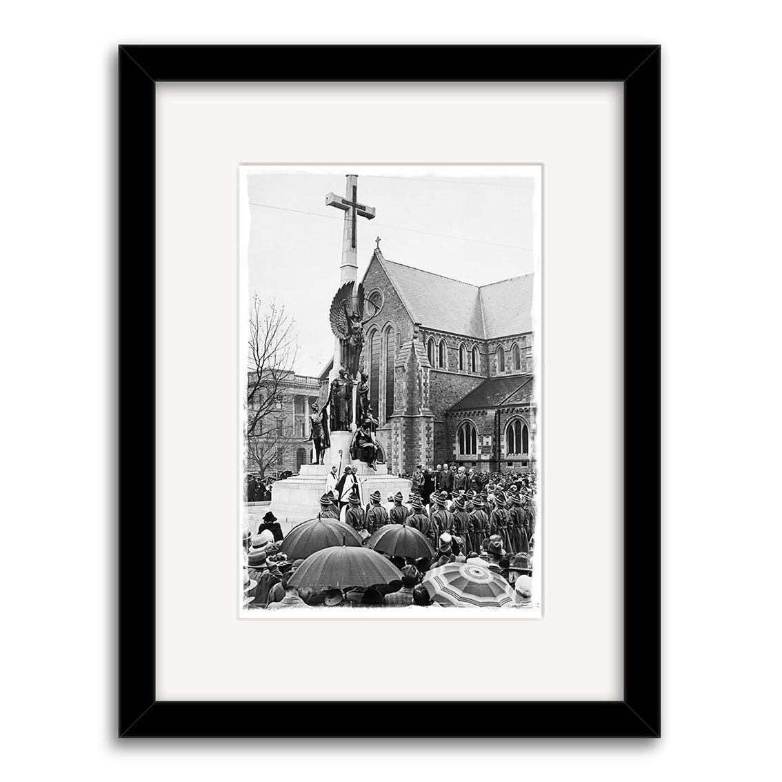 War Memorial 1937 - HI208: Black and white historical photo print of a crowd outside a stone church by a large cross in New Zealand, people with umbrellas in early 20th-century attire, framed in black with archival quality white mat.