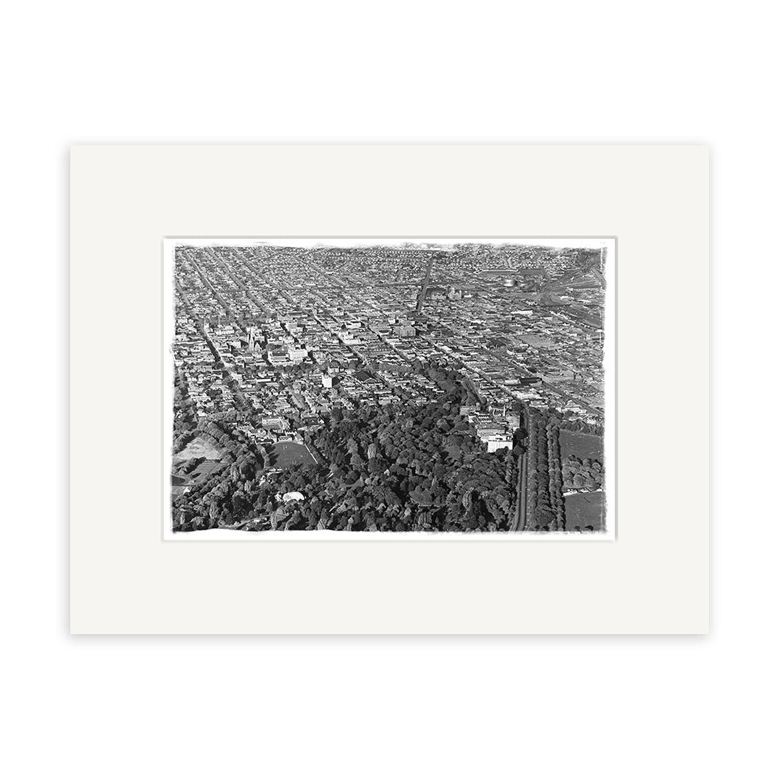 The Christchurch 1950 - HI213 is an archival quality black and white aerial photographic print. It shows a city grid, buildings, and a large tree-filled park in the foreground, matted with a white border.
