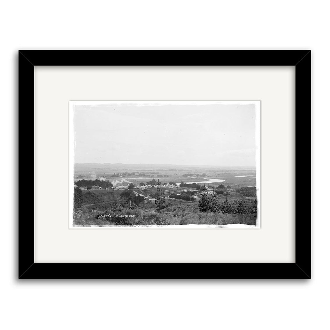 Black-framed, matted Historical Photographic Print titled Helensville 1914 No.1 - HI214, featuring a wide landscape of a small town with scattered buildings, trees, a winding river, and hills in the background. Printed on archival matte paper.