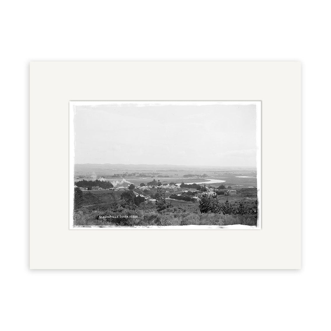 Black and white historical photographic print, Helensville 1914 No.1 - HI214, shows a rural New Zealand town with scattered buildings, a winding river, and distant hills; printed on archival matte paper with a white mat.