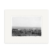 Black and white historical photographic print, Helensville 1914 No.1 - HI214, shows a rural New Zealand town with scattered buildings, a winding river, and distant hills; printed on archival matte paper with a white mat.