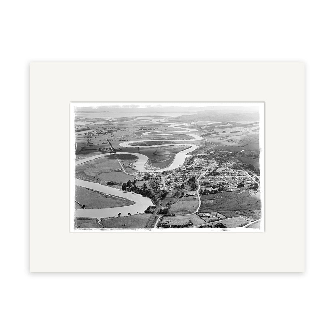 The Helensville 1951 - HI216 archival matte print features a black and white aerial image of a winding river through farmland and a small town, capturing the rural landscapes timeless charm.