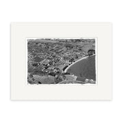Surfdale 1951 No.1 - HI219 is a black and white aerial photograph of a New Zealand coastal town with houses, winding roads, and a curved sandy beach. The historical print is matted with a white border for archival display.