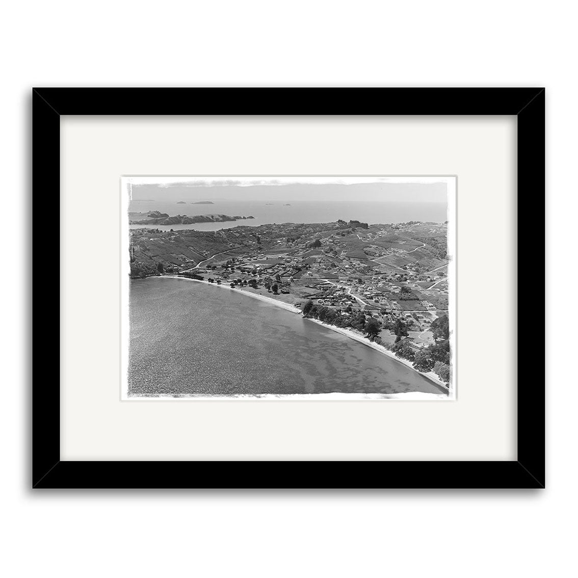 Surfdale 1951 No.2 - HI220 is a black-and-white aerial photo in a black frame showing coastal New Zealand with curved shoreline, buildings, fields, and distant islands. Archival quality with a white mat for display.