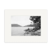 Archival-quality black and white photographic print, Awaroa Bay 1920 - HI222: features New Zealand shoreline, people on rocky ground near water, trees on the right, and hills in the background—a glimpse into the past.