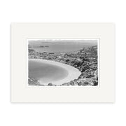 Oneroa Waiheke 1961 - HI223: Black and white aerial photo of a New Zealand coastal town with a curved beach, hills, houses, and roads. Printed on archival paper with a white mat.