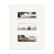 The Coromandel Triptych - RP124 features three black-and-white New Zealand coastal prints in a vertical white matte frame, each showcasing rocks, water, and landforms on archival quality matte paper.