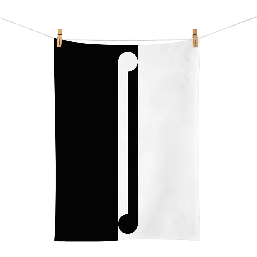 The Gordon Walters - Maho Tea Towel, featuring a black and white split design inspired by the New Zealand artist, hangs from a clothesline with clothespins and is divided vertically by a white bar with rounded ends.