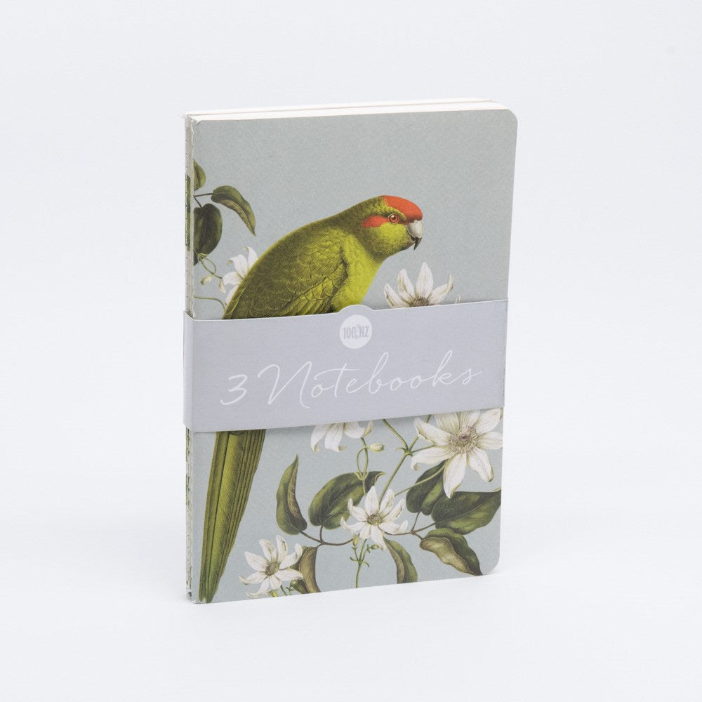 The Birds & Botanicals Notebook Set features a notebook with a green parrot and white flowers on the cover, hand-stitched binding, and a light gray band labeled 3 Notebooks, all displayed against a plain white background.