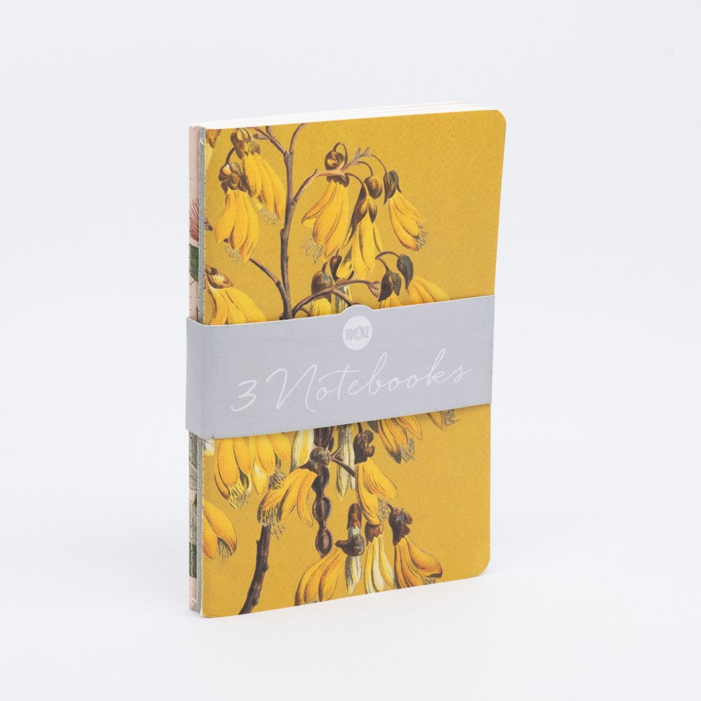 The Vintage Botanicals Notebook Set includes a yellow notebook with yellow flower illustrations on the cover, quality paper, and a gray band labeled 3 Notebooks in white script. The hand-stitched notebook stands upright against a white background.