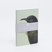 The Hushed Birds Notebook Set includes three hand-stitched notebooks, bound with a gray band labeled 3 Notebooks. The front cover displays an illustration of a dark-feathered bird against a pale background.