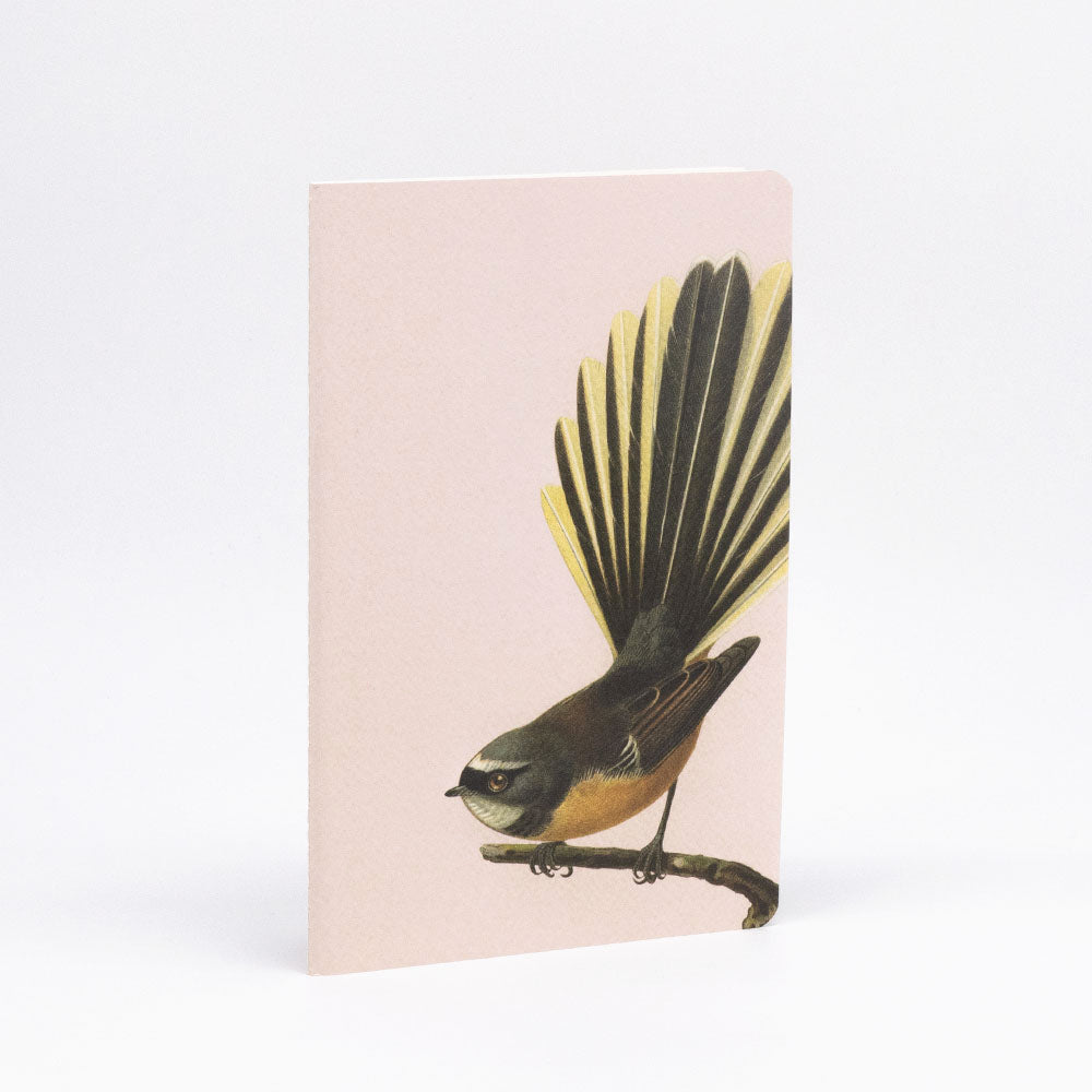 The Hushed Birds Notebook Set features hand-stitched notebooks with light pink covers, white backgrounds, and illustrations of upright, fanned-tail birds perched on branches, all crafted with quality paper.