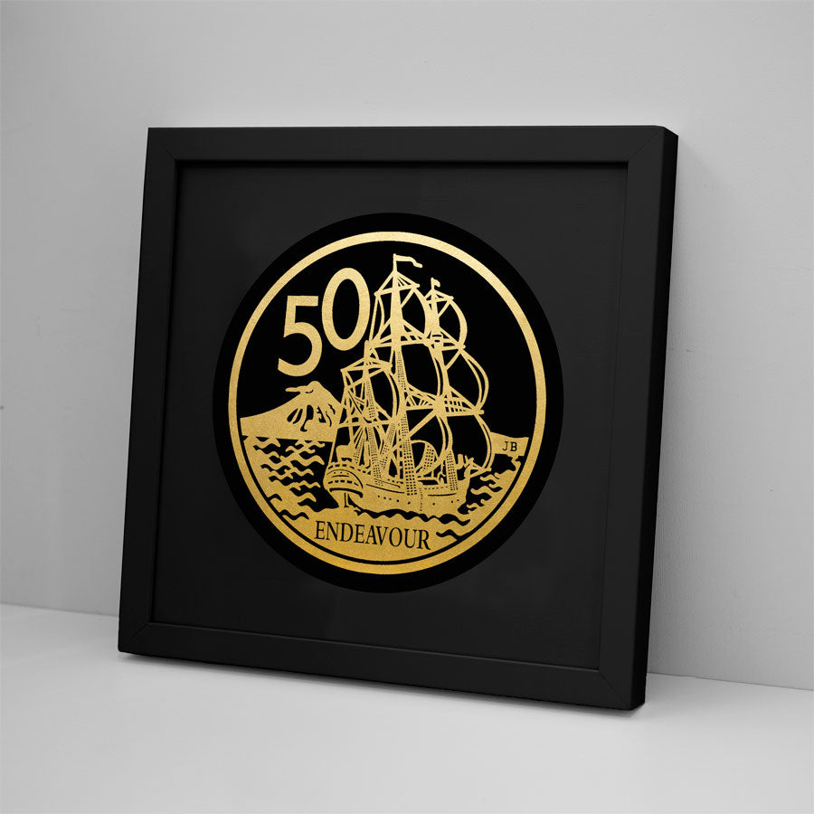 The 50 Cent Coin Foil Print features gold foil Kiwiana artwork of a sailing ship, the number 50, ENDEAVOUR text, and a mountain, framed and leaning against a light gray wall.