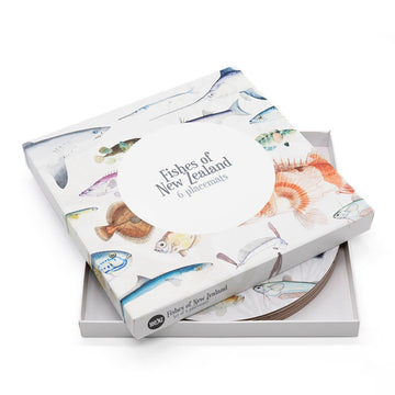 The Fishes of NZ Box of 6 Placemats features illustrated fish on the cover; the box is partially open to show cork-backed placemats inside, each with matching fish artwork. Designed in New Zealand.
