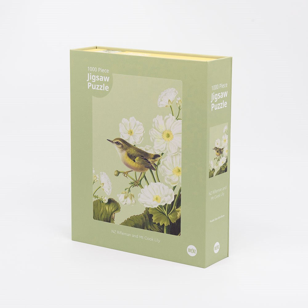 The Rifleman Jigsaw Puzzle Box features 1000 pieces with an illustration of a Rifleman among Mt Cook Lily flowers on a light green background. The puzzle is titled NZ Rifleman and Mt. Cook Lily.